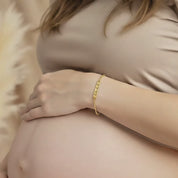 Video showcasing a pregnant mom gently resting her hand on her baby bump while wearing a custom engraved heartbeat bar bracelet in shiny yellow gold, featuring a delicate chain and minimalist heartbeat line design across the bar; sentimental maternity jewelry gift for expecting mom or new mom, perfect for baby shower, pregnancy announcement, push present or Mother’s Day, modern and elegant everyday bracelet.