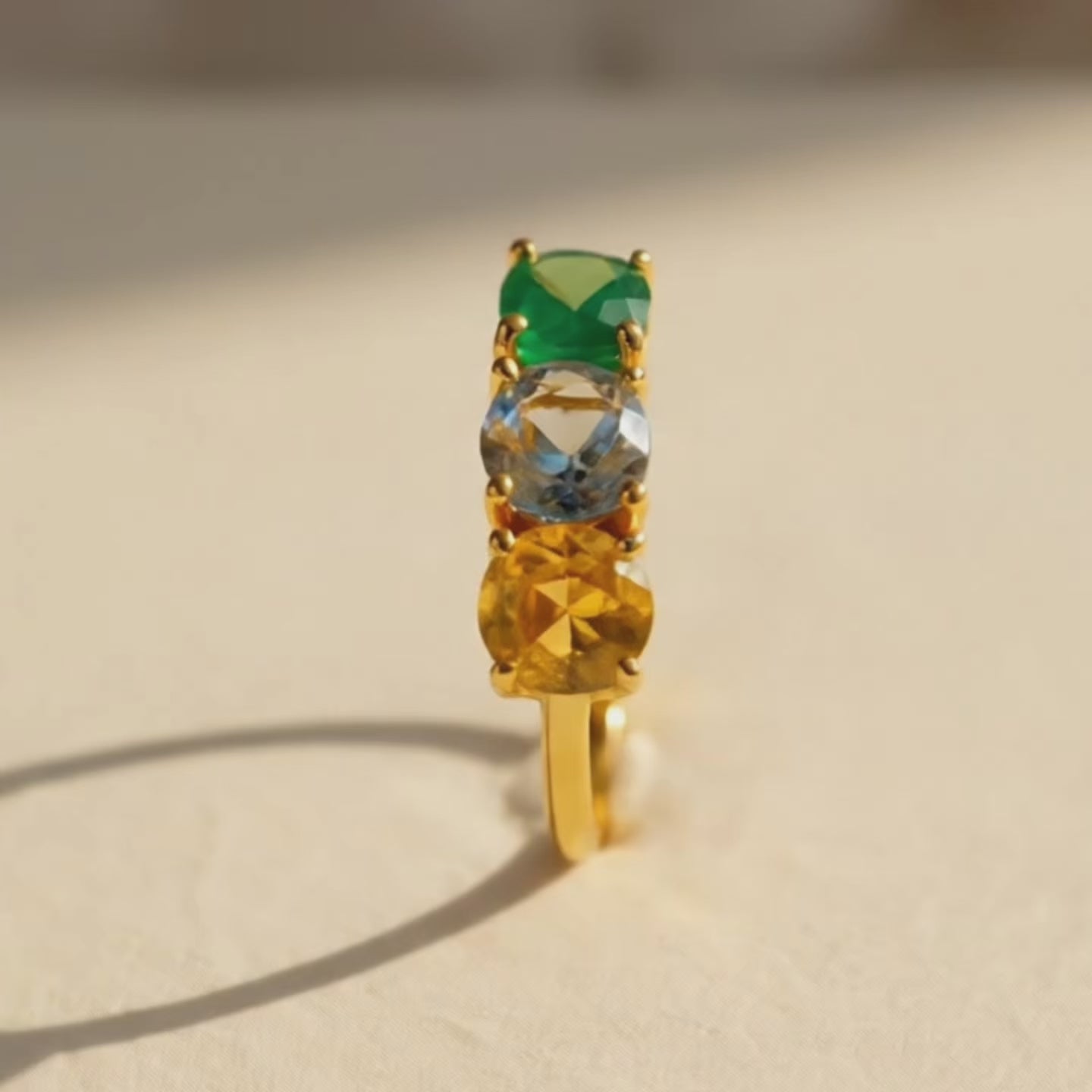 Video showcasing a personalized mom ring with three birthstones in a vertical setting, featuring green, blue, and yellow gemstones on a gold band in warm natural light.