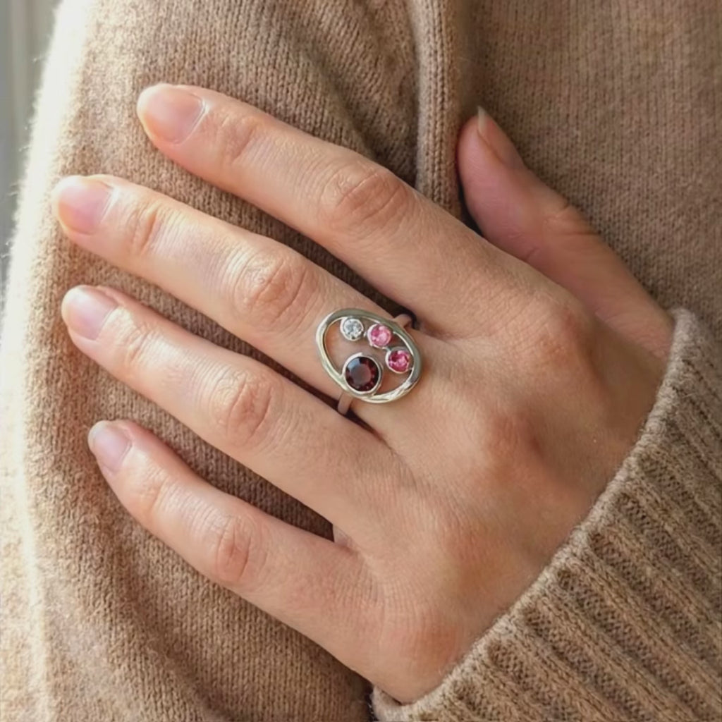 A shot of multiple birthstone rings in a ring tray and an open danique jewelry box. A person tries one on.This delicate egg shaped piece can be set with your choice of birthstone, with gemstone options for every month, plus alternative options if you want something a little different. Rings are available in gold, rose gold, or sterling silver and are hand crafted to your unique style. Birthstones available for January, February, March, April, May, June, July, August, September, October, November, December. 