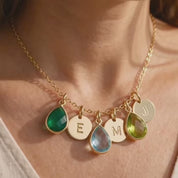 A video showcasing a Custom mom birthstone necklace with green, blue, and peridot teardrop charms and gold initial discs on a warm neutral background.