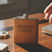 Video showcasing personalized leather-wrapped stainless steel flasks engraved with names, initials and wedding titles, displayed in a warm fireplace setting to highlight custom monogram options, rustic groomsmen gift appeal, and premium handcrafted craftsmanship.