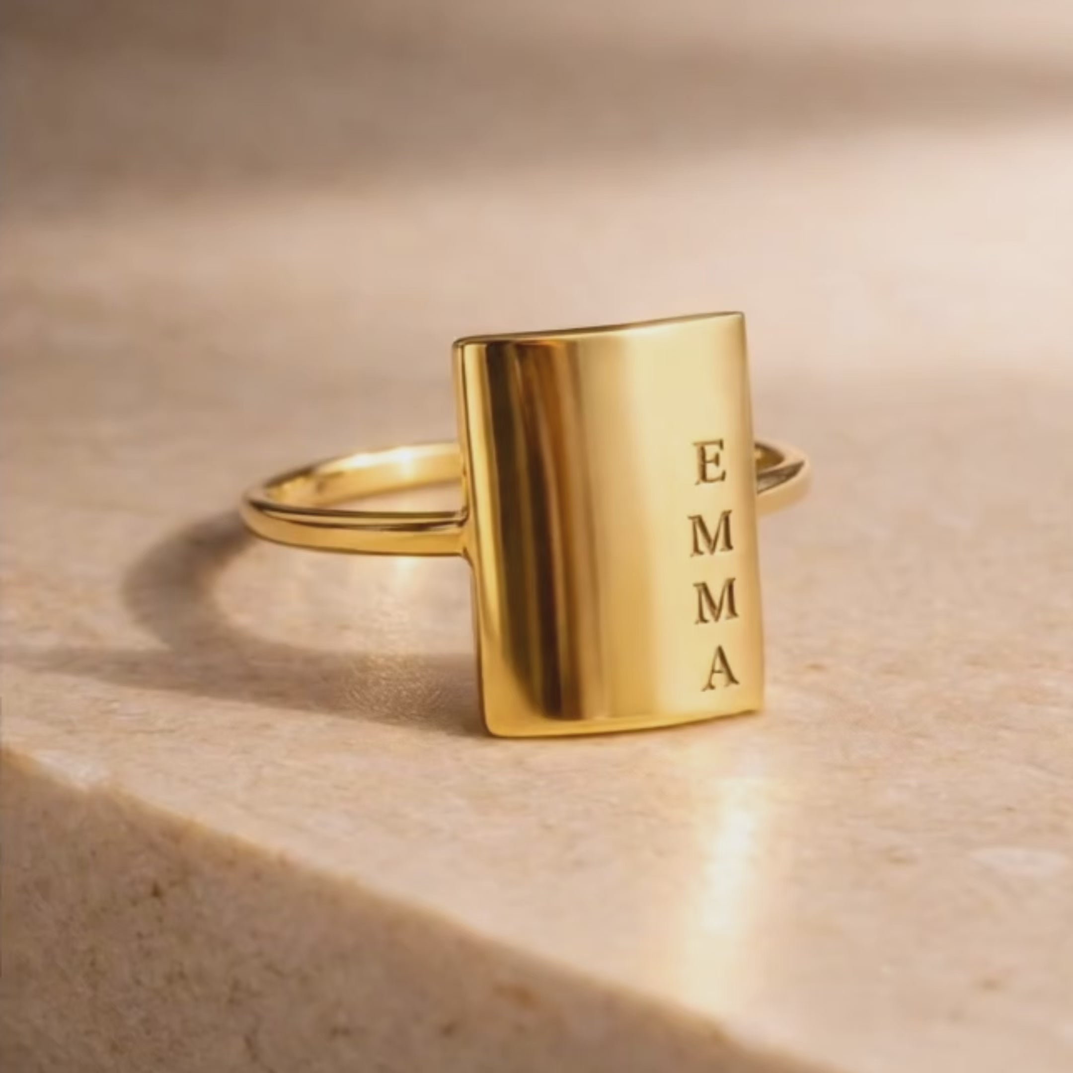Custom engraved rectangular gold ring video showcasing personalized vertical name engraving, minimalist signet style bar ring with smooth polished finish, custom name ring for women, modern gold statement ring with engraved letters, dainty stacking ring personalized gift for mom or grandma, elegant everyday personalized jewelry in warm neutral setting