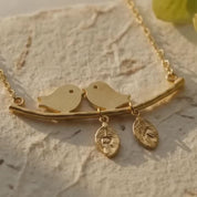 A video showcasing Gold or silver personalized lovebirds necklace with two hand-stamped leaf initial charms on warm beige linen.