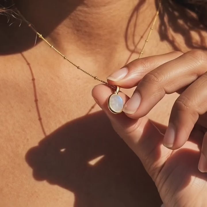 A video showcasing a Mother of Pearl oval pendant necklace in gold shown on soft cream fabric in natural sunlight.