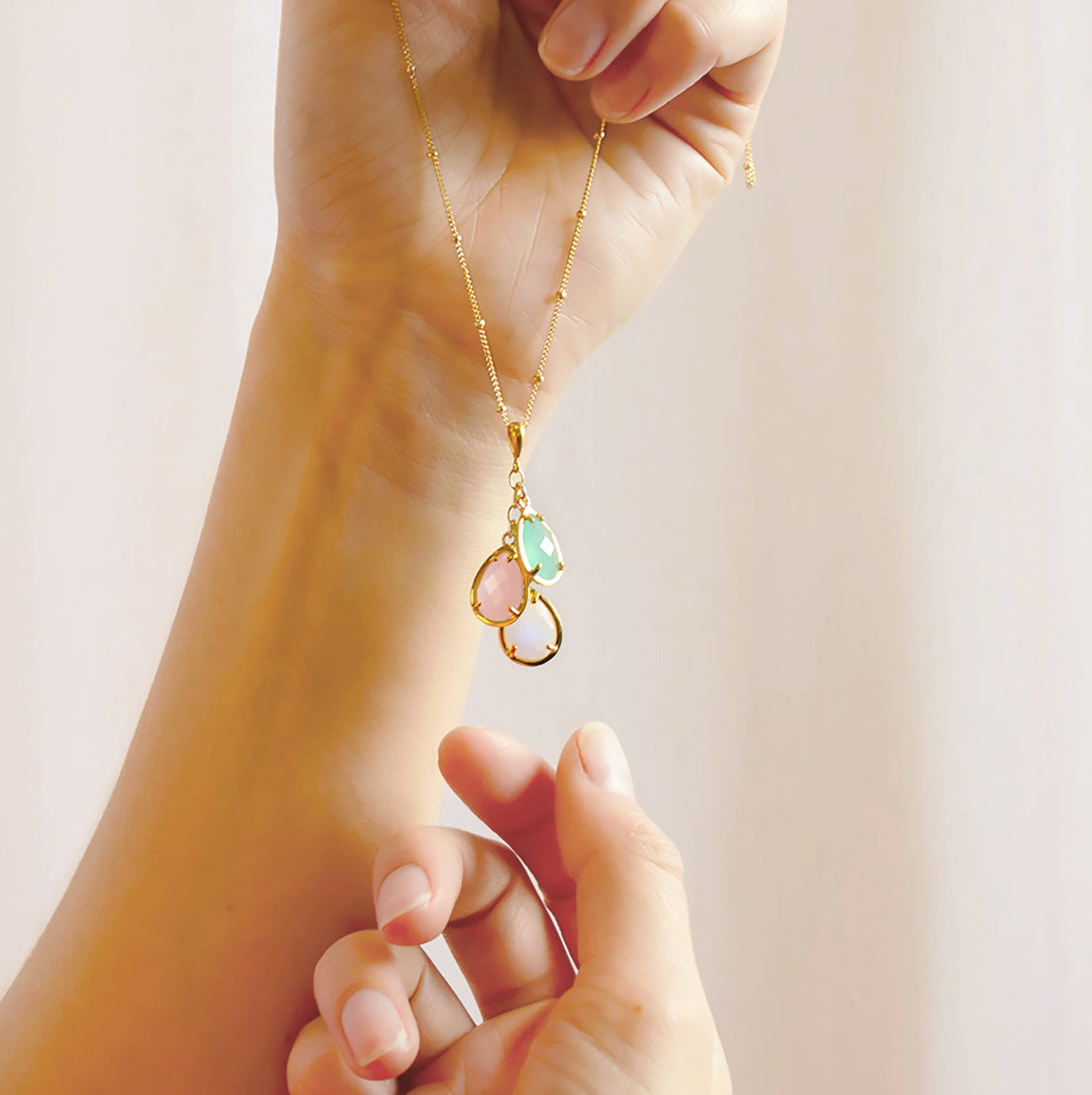 Close-up of hand gently holding a custom teardrop birthstone mom necklace, highlighting the size, movement, and fine detailing of the prong-set stones and delicate chain. Personalized family birthstone pendant that can be customized with multiple birthstones, a unique Mother’s Day, birthday, or Christmas gift idea for mom or grandmother who cherishes her children and grandchildren.