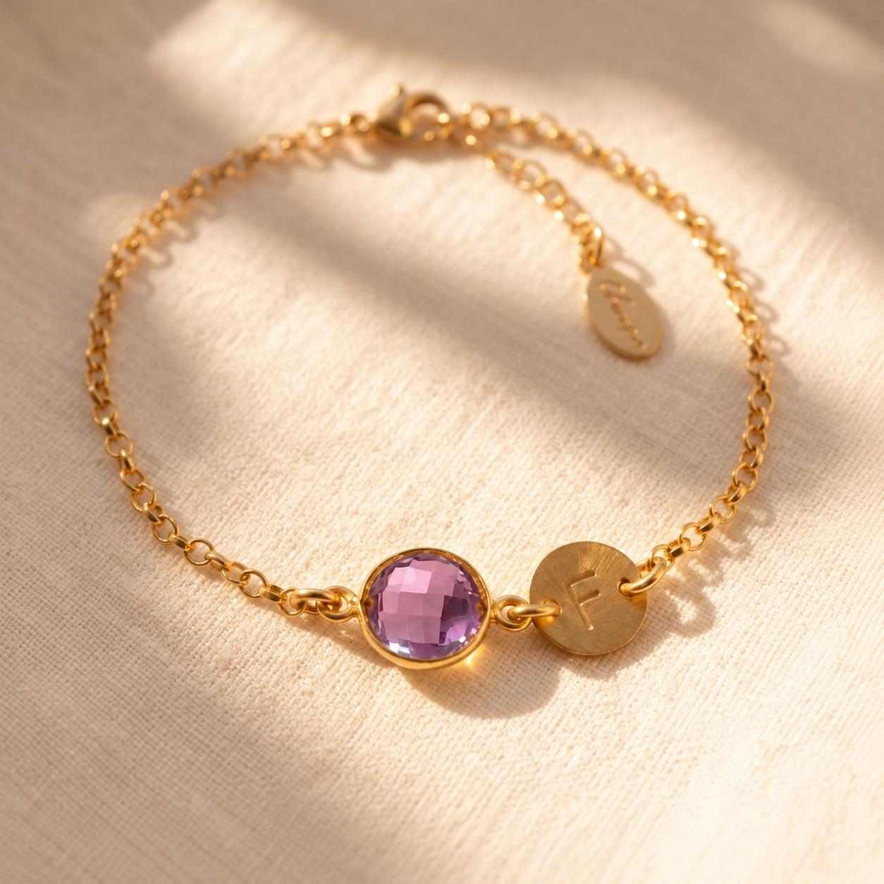 Personalized purple amethyst bracelet with round February birthstone and initial charm on a delicate gold chain.
