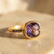 Cushion cut purple amethyst pave ring in yellow gold with faceted gemstone and sparkling accent band.