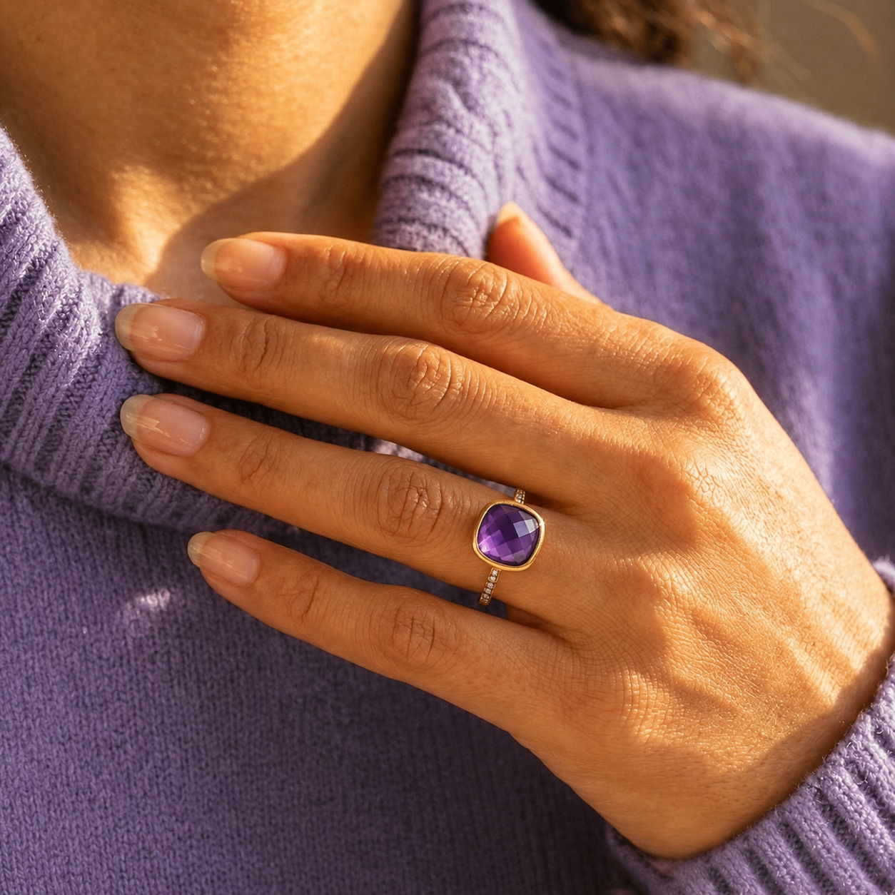 Woman wearing a gold cushion amethyst February birthstone ring with a lavender sweater.