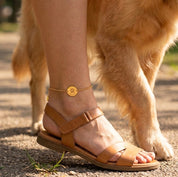 Woman wearing personalized gold paw print anklet while standing beside her dog
