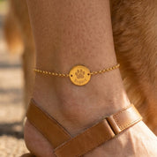 Woman wearing personalized gold paw print anklet engraved with pet name on ankle