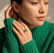Woman wearing a teardrop emerald ring with matching green gemstone earrings, styled with a rich emerald sweater.