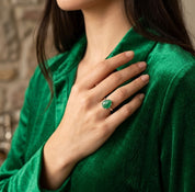Woman wearing the natural emerald ring with a green blouse, showing the teardrop gemstone in an elegant lifestyle setting.