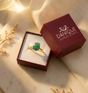 Natural emerald teardrop ring displayed in a Danique Jewelry gift box beside branded packaging and dried flowers.