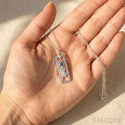 Custom family birthstone necklace held in hand, featuring a vertical silver bar pendant with colorful gemstones.