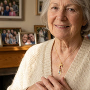 Grandma wearing a personalized birthstone bar necklace with family photos behind her, sentimental gift with kids or grandkids birthstones.