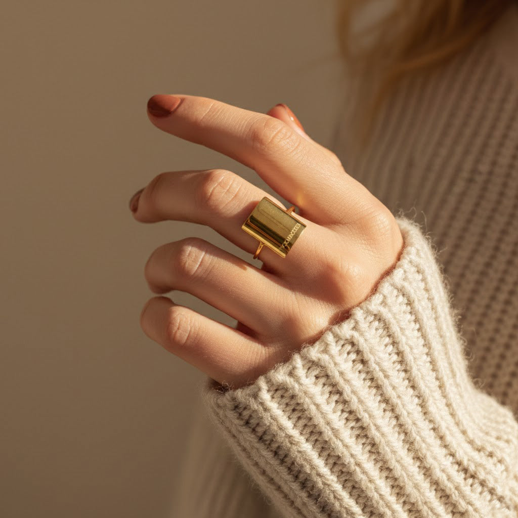 Model in white sweater is wearing a gold plated engraved rectangle nameplate ring. name plate ring, bar, statement ring. 