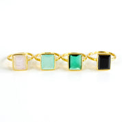 Four Large Rectangle Gemstone Rings in Vermeil Gold Lined up diagonally on a white background. Black Onyx Rectangle Ring, Green Emerald Quartz May Birthstone Ring, Aqua Chalcedony March Birthstone Ring, and Rainbow Moonstone June Birthstone Ring
