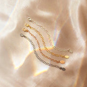 Necklace extender chains in gold, silver, and rose gold displayed on satin fabric background. Jewelry accessory adds 1–6 inches to necklace or bracelet for layering styles. Popular gift upgrade for birthdays, Christmas, or bridesmaids.