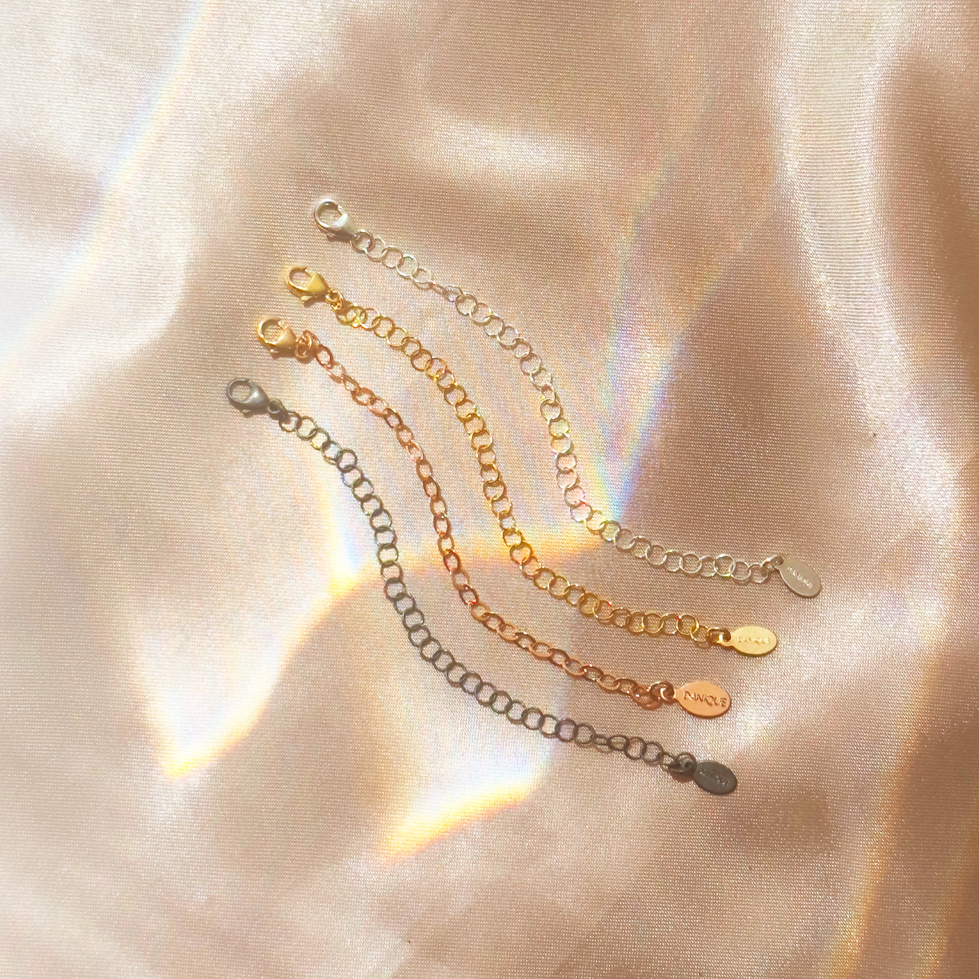 Necklace extender chains in gold, silver, and rose gold displayed on satin fabric background. Jewelry accessory adds 1–6 inches to necklace or bracelet for layering styles. Popular gift upgrade for birthdays, Christmas, or bridesmaids.