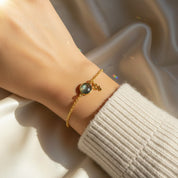 Woman wearing a personalized birthstone initial bracelet with a deep blue bezel-set gemstone and delicate gold script initial charm, styled on a dainty gold chain against soft satin light reflections. This custom birthstone bracelet is available in 18K gold vermeil, rose gold or sterling silver and makes a meaningful gift for mom, daughter, sister or best friend. Perfect for birthdays, Mother’s Day, Christmas or bridesmaid jewelry with elegant minimalist style.