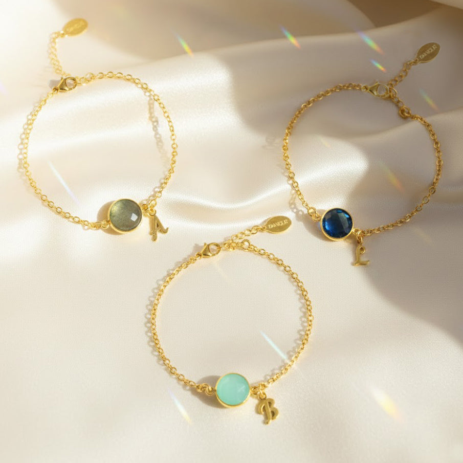 Dainty personalized birthstone initial bracelets displayed on soft satin fabric, featuring bezel-set medium round gemstones in aqua, labradorite and deep blue tones paired with gold script initial charms. These personalized birthstone initial bracelets are available in sterling silver or 18K gold vermeil and make meaningful gifts for mom, daughter, best friend or bridesmaids. A beautiful custom jewelry option for birthdays, Christmas, Mother’s Day or everyday stacking.