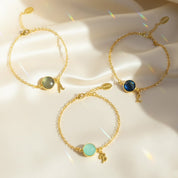 Dainty personalized birthstone initial bracelets displayed on soft satin fabric, featuring bezel-set medium round gemstones in aqua, labradorite and deep blue tones paired with gold script initial charms. These personalized birthstone initial bracelets are available in sterling silver or 18K gold vermeil and make meaningful gifts for mom, daughter, best friend or bridesmaids. A beautiful custom jewelry option for birthdays, Christmas, Mother’s Day or everyday stacking.
