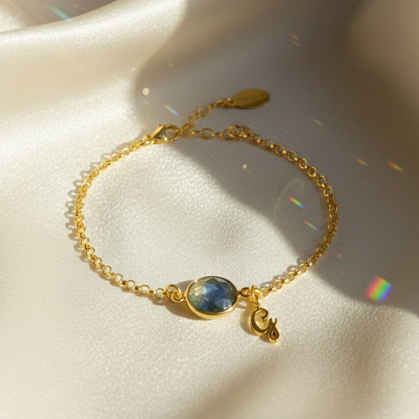 Close-up of a personalized birthstone initial bracelet featuring a labradorite bezel-set gemstone with iridescent blue-green tones paired with a dainty gold script initial charm. Set on an 18K gold vermeil chain with extender, this custom bracelet offers modern minimalist elegance. A beautiful personalized jewelry gift for mom, daughter or best friend, perfect for birthdays, Christmas, Mother’s Day or everyday stacking with other fine gold bracelets.