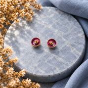 Madgenta and gold abstract flower stud earrings displayed on dark textured stone