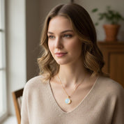 A glowing opalite pendant necklace worn by a woman in soft natural light, highlighting the gemstone’s milky iridescence and gold chain. A perfect dainty necklace for bridesmaids, weddings, birthdays, or everyday minimalist jewelry. Trendy modern opalite style ideal for stacking, layering, and personalized gemstone gifting.
