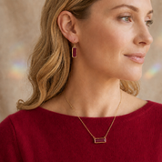 Model wearing a dainty ruby baguette birthstone necklace with matching ruby earrings.