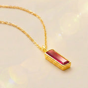 Gold necklace with a red ruby July birthstone bar pendant on a beige background