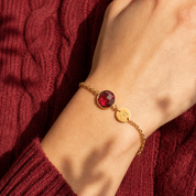 Ruby birthstone initial bracelet worn against a soft burgundy sweater