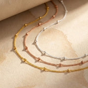 Dew Drops choker necklace photographed in yellow gold filled finish, laid in soft natural light to showcase the delicate satellite beads, thin chain design, and handcrafted quality of this minimalist jewelry piece