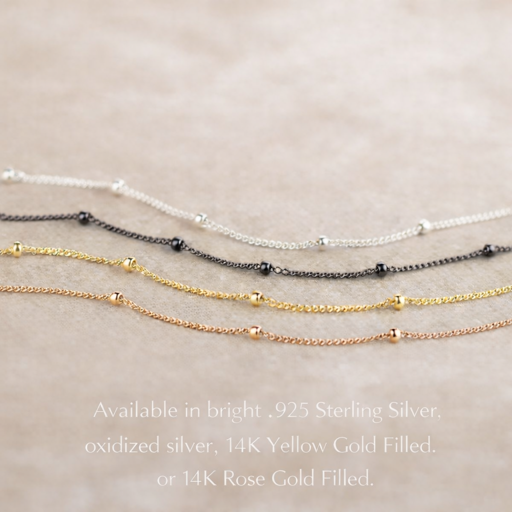 Close-up of the Dew Drops satellite chain necklace displaying oxidized silver, sterling silver, yellow gold filled, and rose gold filled finishes side by side, emphasizing the subtle bead accents and refined minimalist design