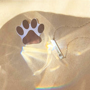 Sterling Silver bar necklace engraved with the name “Moose” and a paw symbol, displayed beside a paper paw cutout on a warm beige background with rainbow light reflections. Personalized pet lover jewelry available in gold filled, sterling silver, or rose gold filled. Custom bar necklace with engraved paw and pet name, perfect for gifts for dog moms, cat owners, and as a memorial keepsake for animal lovers.