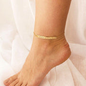 Woman wearing a gold personalized bar anklet with a slim engraved 3 by 40 mm plate.