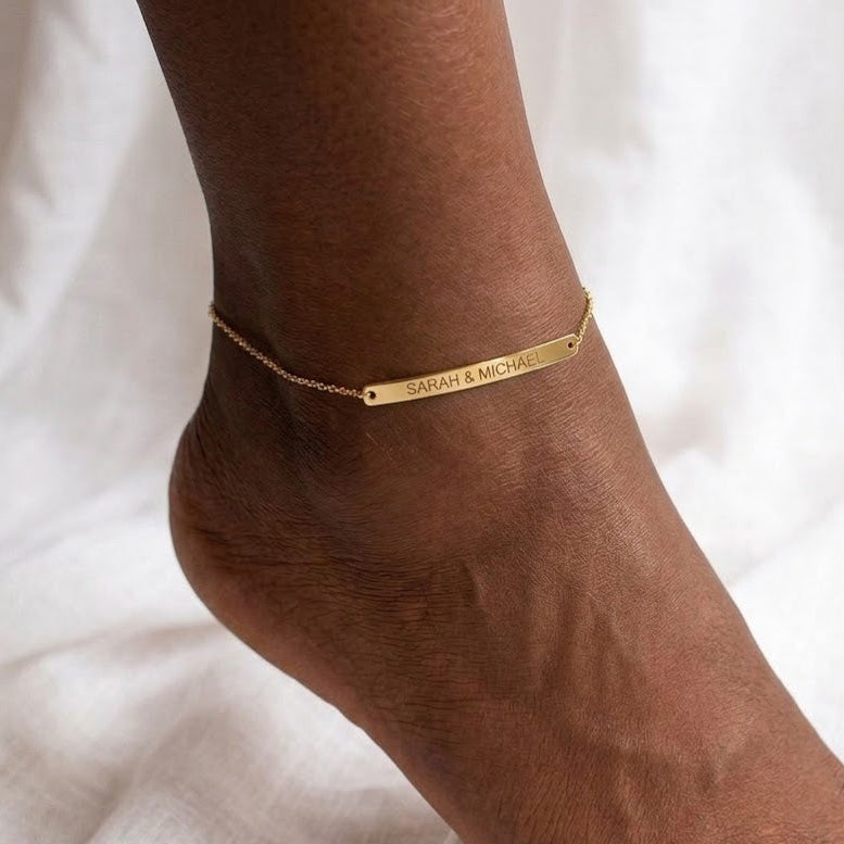Woman wearing a personalized gold skinny bar anklet engraved with a custom name on her ankle.