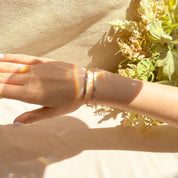 Dainty layered Morse code skinny bar bracelets on a woman’s wrist in warm sunlight, slim gold and silver bars catching rainbow reflections, minimalist personalized bar bracelet design with delicate chains that can be engraved with a hidden morse code message, perfect stacking bracelet for everyday wear, meaningful custom gift for mom, sister, best friend or bridesmaid, available in .925 sterling silver, 14k yellow or rose gold filled for birthdays, anniversaries or Christmas.