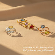 Flat lay of stacking birthstone rings arranged on neutral fabric, colorful oval January Garnet, March Aquamarine, April Diamond Clear Quartz in gold and silver bands, minimalist birthstone ring collection for women who love layered jewelry