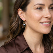 Woman wearing large round Smoky Quartz drop earrings in gold with warm brown faceted gemstones.
