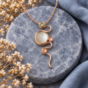 Sage and peach boho serpentine necklace with rose gold swirl pendant on gray stone

