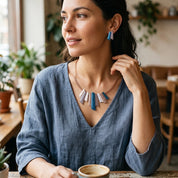 Woman wearing Modernist Fan geometric necklace and matching blue stud earrings in cafe setting

