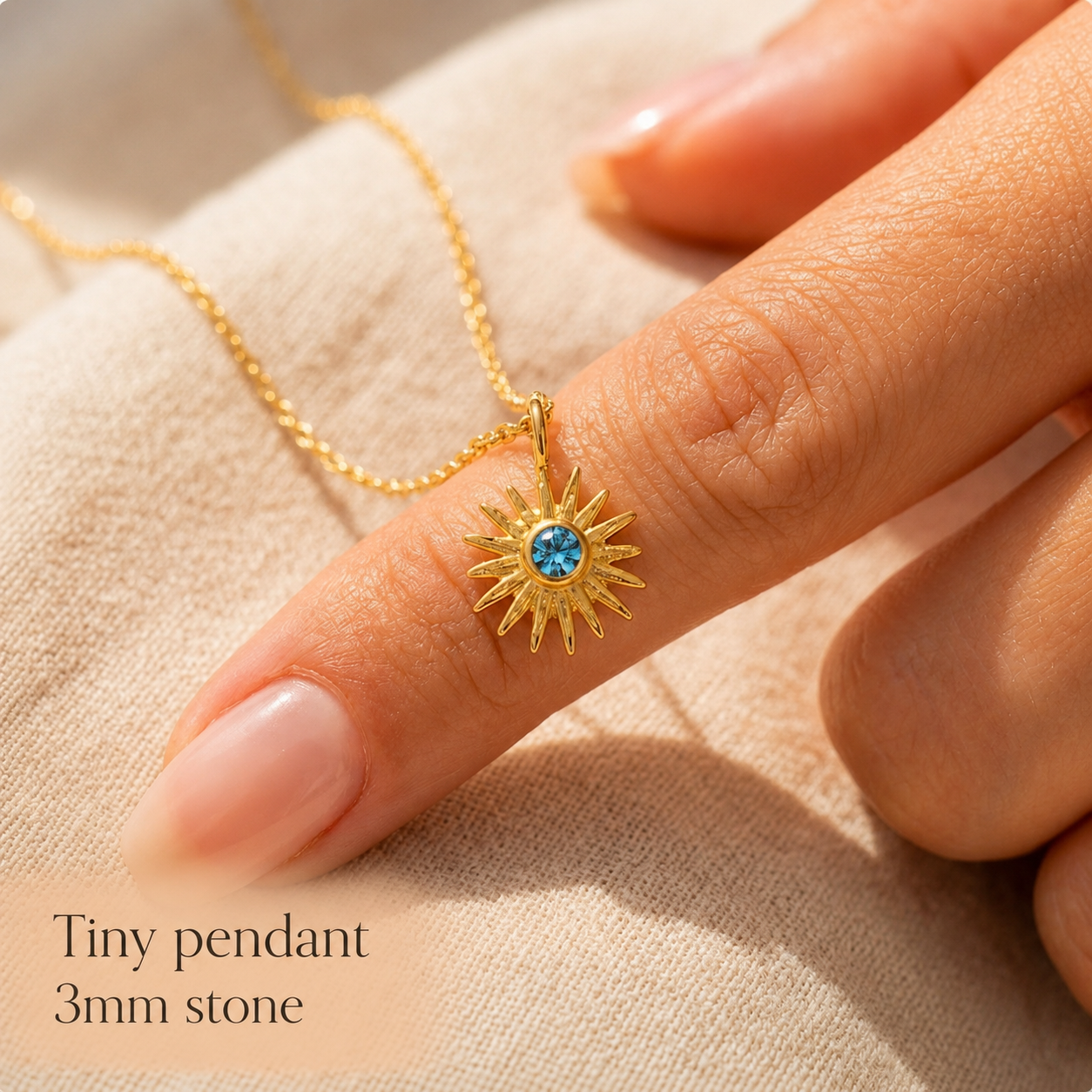 Close-up of a tiny 3mm birthstone pendant on a gold chain beside a finger for scale, showing the petite size of the gemstone necklace.