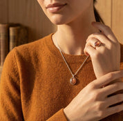Model wearing a sunstone necklace with a rust-colored sweater, showing the dainty pendant length and warm gemstone tone.