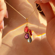 Close-up of a three-stone teardrop cluster pendant, customized with family birthstones on a delicate satellite chain; a custom birthstone necklace that’s perfect as a mothers birthstone necklace or push present. Shown in warm gold tones with shimmering hydro-quartz/chalcedony options for kids’ months (January–December). A meaningful layered birthstone necklace and everyday mom necklace gift.