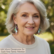 Woman with gray hair and earrings against a blurred natural background. Personalized family earrings with natural hydro-quartz and chalcedony birthstones, available in all twelve birth month colors and crafted as a thoughtful Mother’s Day or anniversary gift for her.