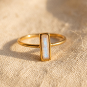 Tiny moonstone bar ring in yellow gold with 10 x 3mm baguette gemstone on linen.