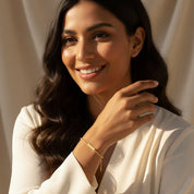 woman smiling while wearing a tiny gold bar bracelet with personalized engraving, styled as a minimalist and elegant everyday accessory, featuring a slim nameplate on a delicate chain, customizable with initials, names or dates in your choice of font, available in sterling silver or 18k gold vermeil, perfect gift for birthdays, bridesmaids, anniversaries or meaningful custom jewelry for mom, daughter or best friend