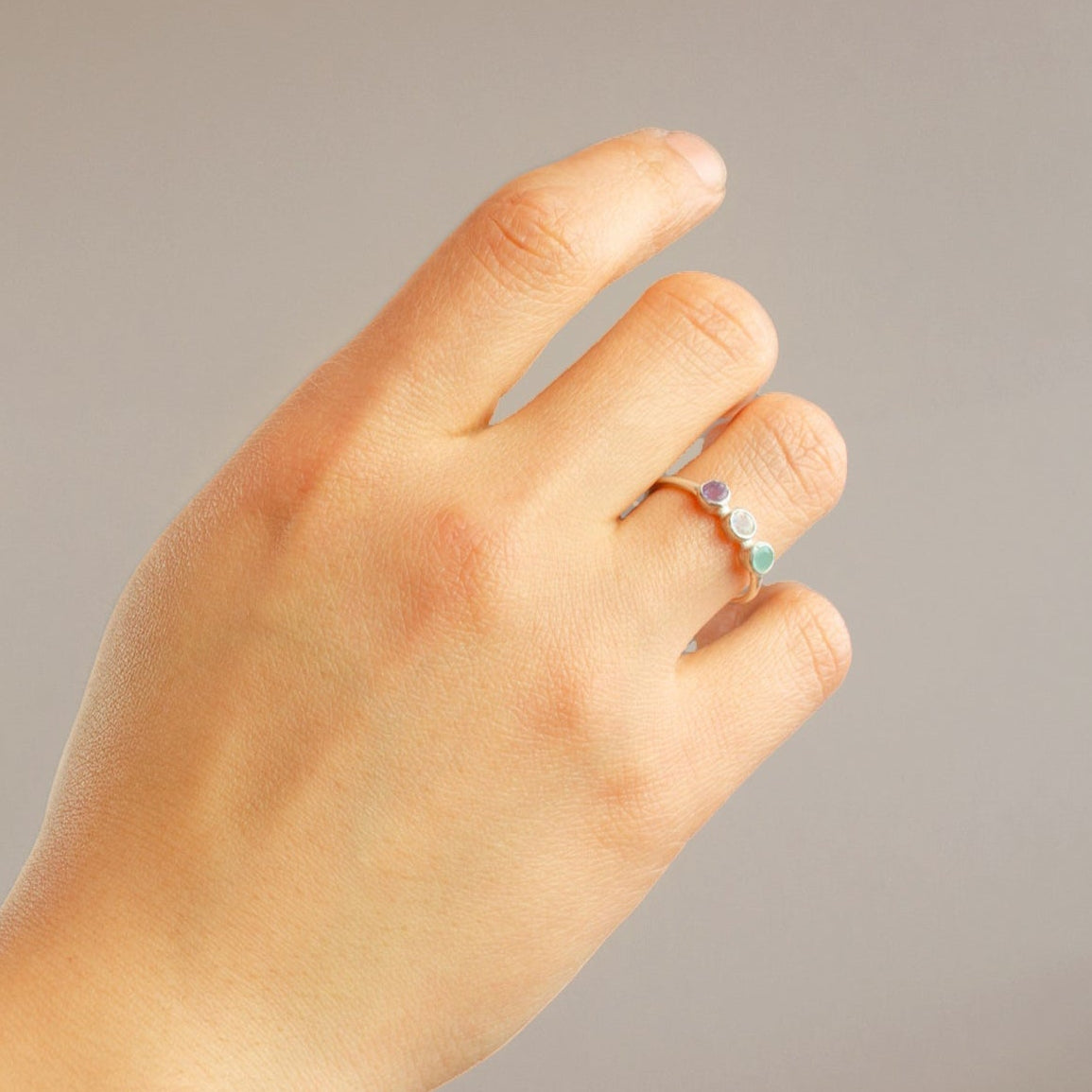 Triple Birthstone Ring for mom on models hand. Great gift for Christmas in Vermeil Gold on a white background. Personalized Birthstone Rings for Mom of three, Perfect gift for Mother's Day. December Birthstone, November Birthstone, and September Birthstone Dainty Bezel Set Ring. January Birthstone, June Birthstone, and February Birthstone Custom Ring with Kids Birthstones. Blue Topaz, Citrine and Kyanite Ring. Garnet, Rainbow Moonstone, and Purple Amethyst Ring
