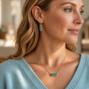 Woman wearing a personalized turquoise bar necklace with engraved rectangular gemstone pendant on a delicate gold chain.